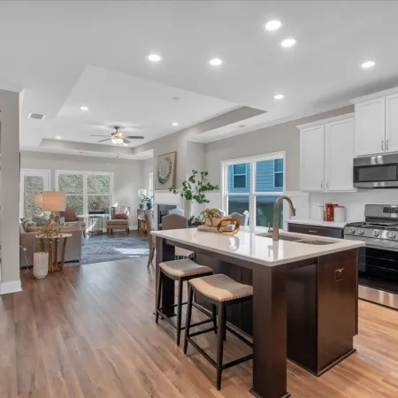 Modern open-concept kitchen and living area with hardwood floors, white cabinets, and a central island with stools.