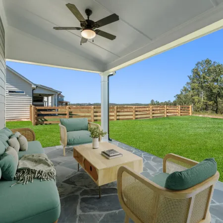 Covered patio with teal cushioned seating, stone floor, wooden table, ceiling fan, and fenced green backyard