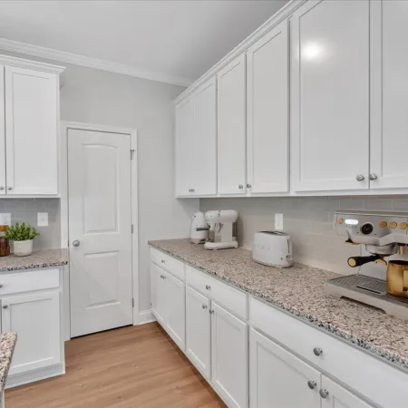 Modern kitchen with white cabinets, granite countertops, espresso machine, toaster, and hardwood flooring.