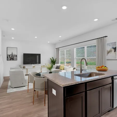 Modern kitchen with dark cabinets and granite countertop, featuring a bright living area with large windows.