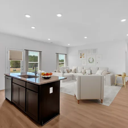 Bright open living room and kitchen with white walls, hardwood floors, dark island, and beige sectional sofa.