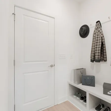 Minimalist entryway with white walls, coats on hooks, a hat, shoes on shelves, and a Nike shoebox on a bench.