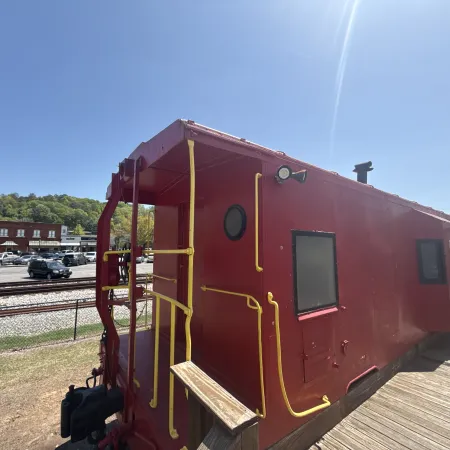 A bright red caboose resting on a sunny day near a railway track and buildings in the background.