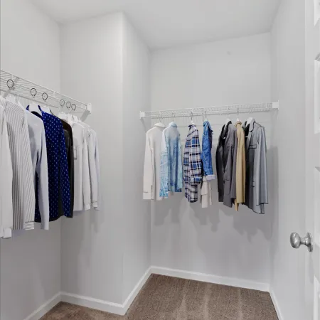 Bright walk-in closet with wire shelving and a variety of hanging shirts and jackets on a carpeted floor.