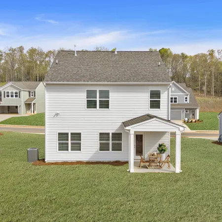 Backyard view of a modern two-story white house with a small covered patio and green lawn under a blue sky
