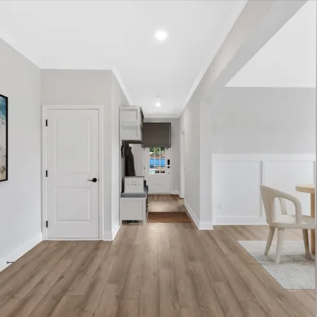 Modern hallway with wood flooring, white walls, abstract wall art, and a glimpse of dining area with light furniture.