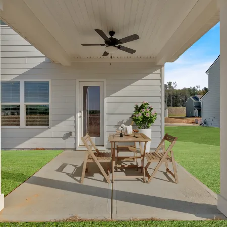 Covered patio with wooden table and chairs, ceiling fan, and potted plant outside a modern house.
