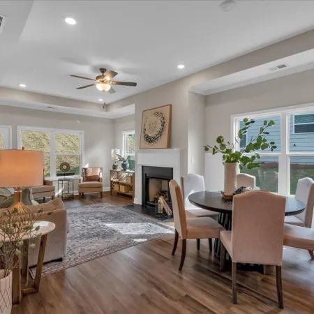 Modern living and dining area with wood floors, neutral furniture, large windows, and ceiling fan lighting.