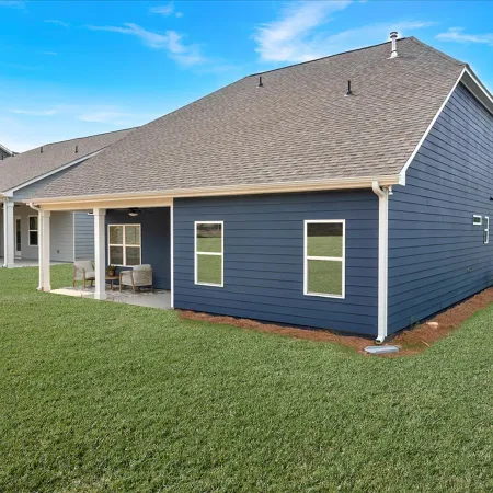 Modern blue house with a covered back patio and well-maintained green lawn under a clear sky