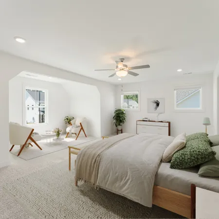 Bright modern bedroom with a wooden bed, cozy seating area, ceiling fan, and framed artwork on white walls.