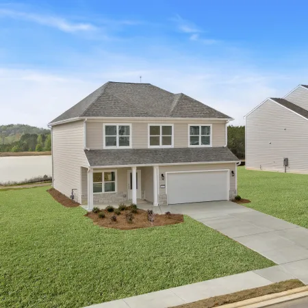 Newly built two-story house with a garage and large green lawn in a suburban neighborhood near a lake.
