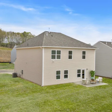 Backyard view of beige suburban homes with patios and green lawns under a clear sky.