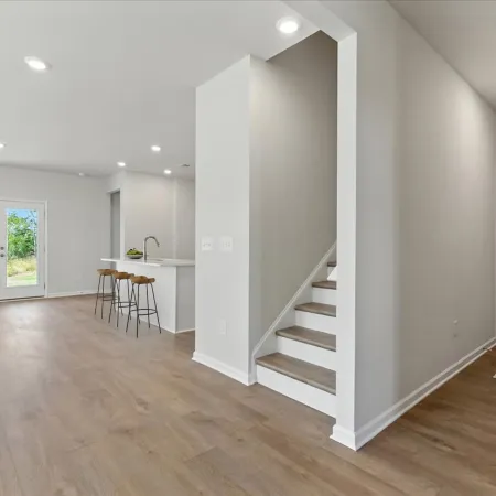 Open living space with staircase, kitchen island with stools, and laundry room with washer and dryer visible