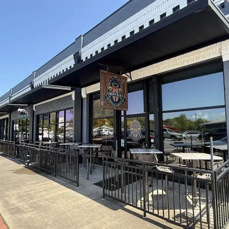 Outdoor seating area of Heavale restaurant with black railings and a wooden hanging sign under a clear blue sky.