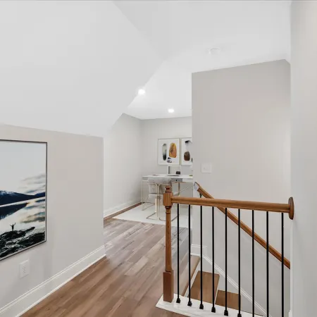 Well-lit hallway leading to a cozy workspace with modern decor and wooden staircase accent.