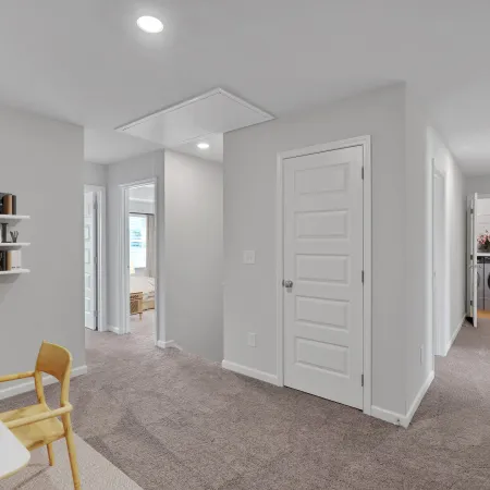 Bright hallway with gray walls, carpeted floor, white doors, and a visible laundry area with washer and dryer.
