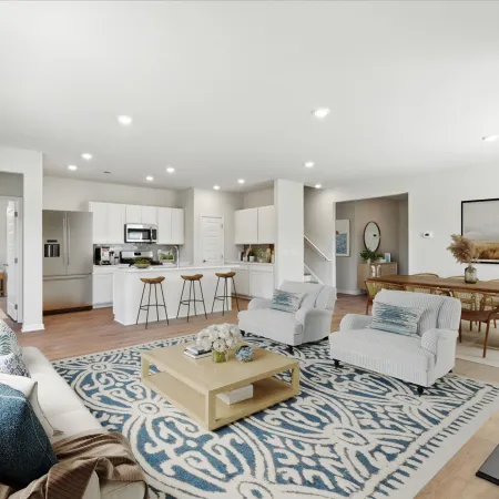 Bright open-concept living space with kitchen, dining area, white furniture, blue patterned rug, and wood flooring.