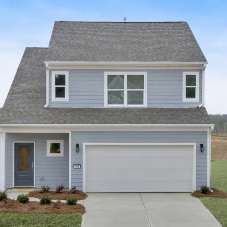 Two-story gray house with white trim, a double garage, front porch, and landscaped lawn under a clear sky.