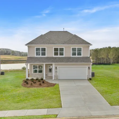 Two-story beige suburban house with a large driveway, green lawn, and clear blue sky in a quiet neighborhood.