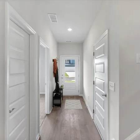 Bright hallway with white doors, light walls, wooden floor, small bench, and stairway with carpet steps.
