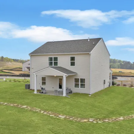 Modern two-story house on a grassy lot with a clear blue sky and surrounding landscape.