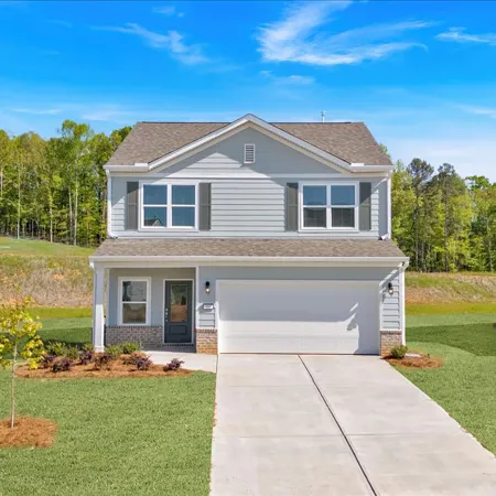 Modern suburban home with a well-manicured lawn and driveway, surrounded by trees under a bright blue sky.