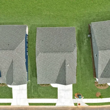 Aerial view of suburban homes with driveways and well-maintained green lawns in a residential neighborhood.