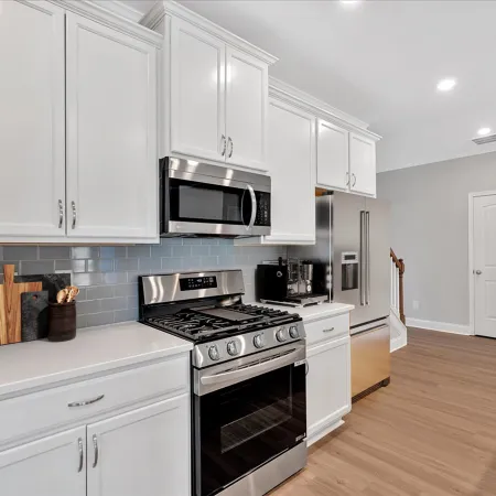 Modern kitchen with white cabinets, stainless steel stove, microwave, refrigerator, gray subway tile backsplash, and wooden floor.