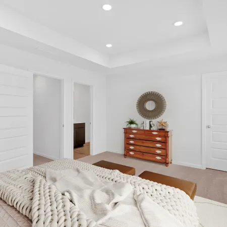 Bright bedroom with white walls, wooden dresser, round mirror, beige knit blanket, and carpeted floor.