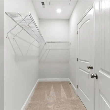 Empty walk-in closet with white wire shelving, beige carpet, white walls, and two closed white doors.