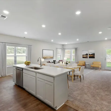 Bright open-concept kitchen and living room with white cabinets, wood floors, carpet, and modern furnishings.