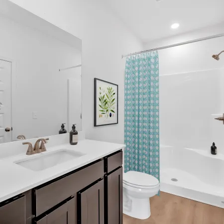 Modern white bathroom with wooden cabinets, blue patterned shower curtain, and green plant decor.