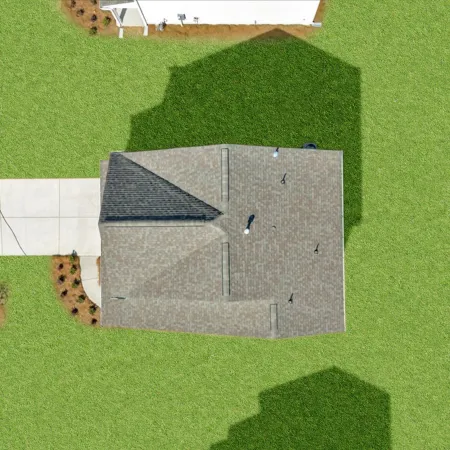 Aerial view of a single house with a gray roof, concrete driveway, and green lawn on a sunny day.