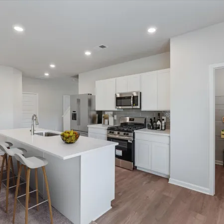 Modern white kitchen with island seating, stainless steel appliances, and pantry with organized shelves.