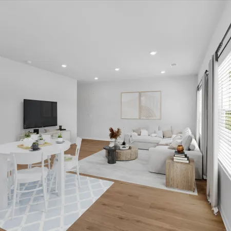 Bright modern living room with white furniture, wooden flooring, round dining table, and large windows with curtains.