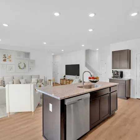 Modern open-concept kitchen and living room with dark wood island, light flooring, and white walls with recessed lighting