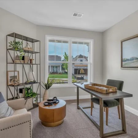 Cozy home office with beige armchair, modern desk, metal bookshelf, large window, and framed landscape painting.