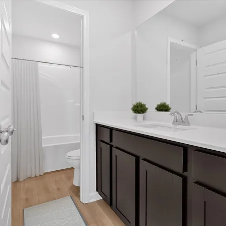 Modern bathroom with dark wood vanity, white countertop, large mirror, and white walls with hardwood floor.