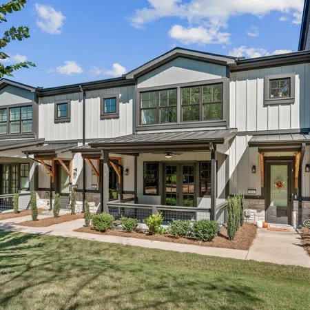 Modern townhouse with white siding, large windows, covered porch, and well-kept landscaping under a blue sky.