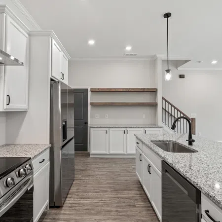 Modern kitchen with granite countertops, stainless steel appliances, white cabinets, and wooden floors under bright lighting