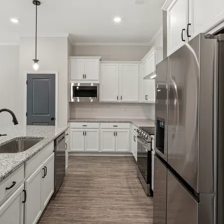 Modern kitchen with white cabinets, granite countertops, stainless steel appliances, and wood flooring under recessed lighting.