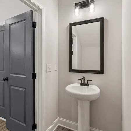 Minimalist bathroom with pedestal sink, black framed mirror, and dark double doors against light walls.