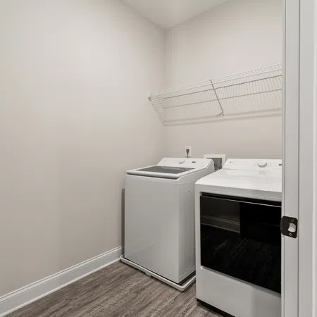Modern laundry room with white washer and dryer units against beige walls and wood-look flooring.