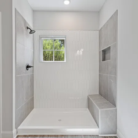 Modern walk-in shower with gray tiles, built-in bench, small window, and white geometric wall tiles.