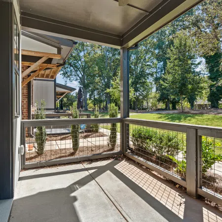 Covered porch with metal railing overlooks green yard and trees under clear blue sky on a sunny day