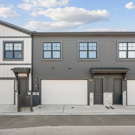 Modern townhouse exterior with gray and white siding, black trim, multiple garages, and clear skies above.
