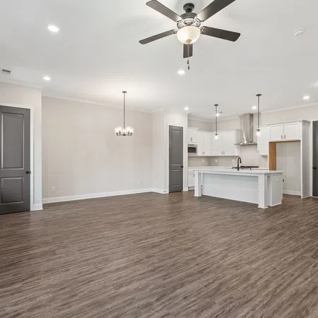 Spacious modern open-concept living room and kitchen with hardwood floors, ceiling fan, and white cabinetry under bright lights.