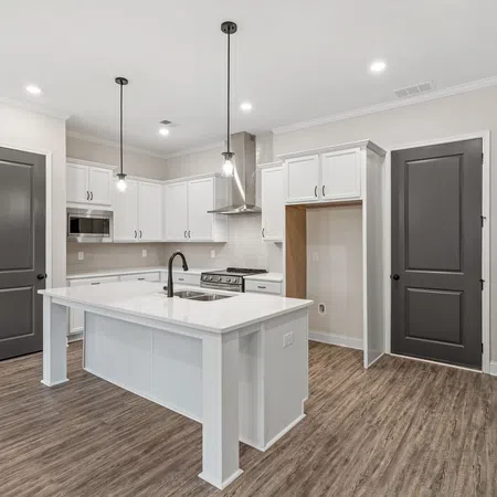Modern kitchen with white cabinets, island with sink, black fixtures, pendant lighting, and wood-style flooring