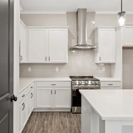 Modern kitchen with white cabinets, stainless steel stove, white countertops, and wood-look flooring under bright lighting