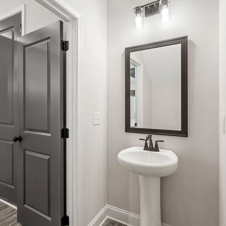 Small modern bathroom with pedestal sink, wall mirror, black framed door, and overhead light fixture.